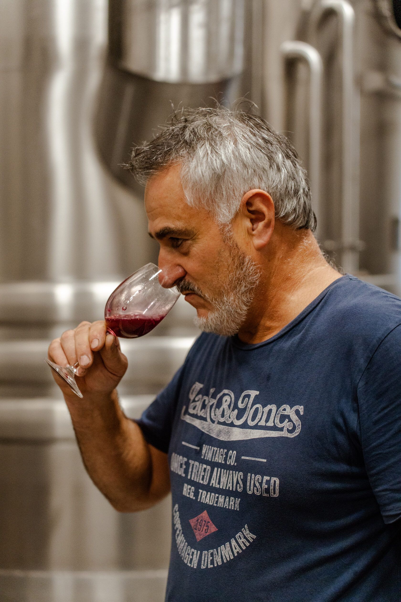 Winemaker tasting red wine at Château Tour des Termes, with steel tanks in the background.
