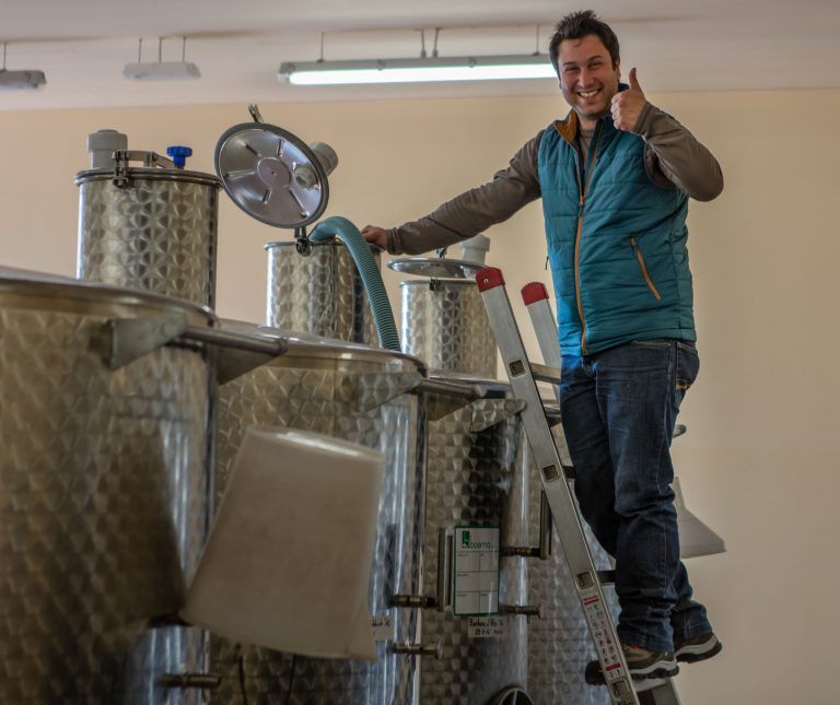 Alberto Voerzio on a ladder by steel tanks gives a thumbs-up.