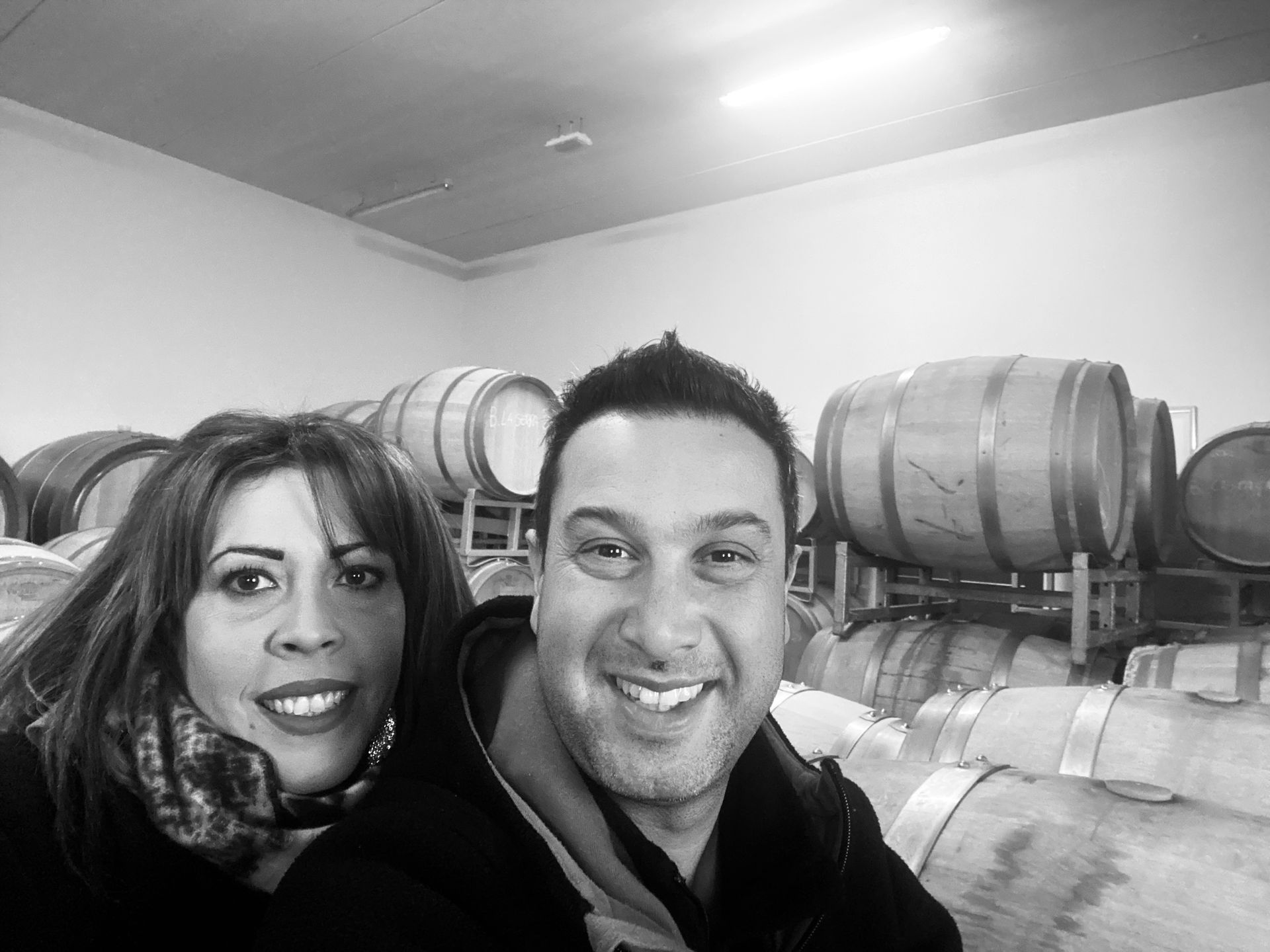 Alberto Voerzio and his wife smiling in front of wine barrels in a cellar.