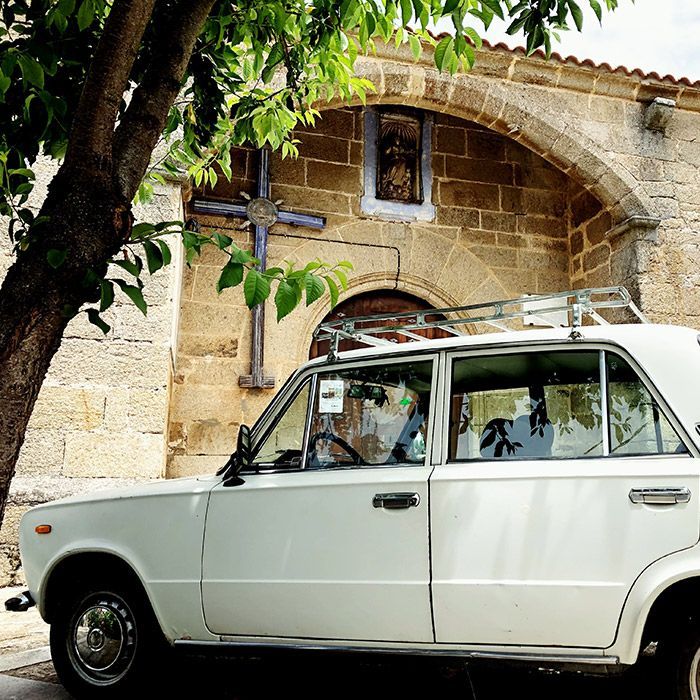 White vintage car parked in front of a stone church with a cross, at Alvar de Dios