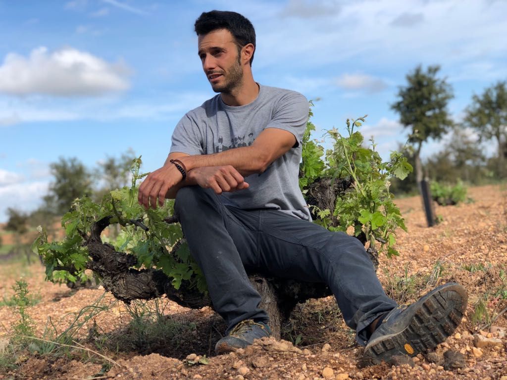 Álvar de Dios winemakers sits near grapevines outdoors, looking off to the side.