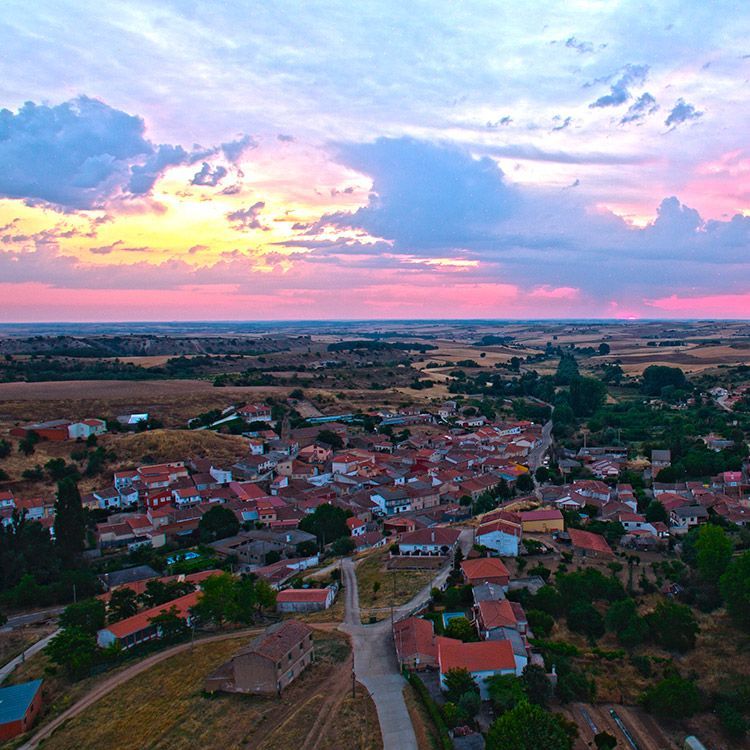 Aerial view of a town with red-tiled roofs under a sunset sky.