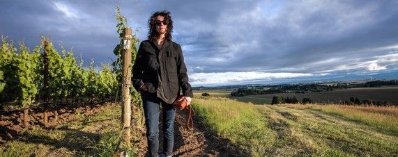 Winemaker of Château Carbonnieux standing in a vineyard, wearing a dark jacket and jeans.