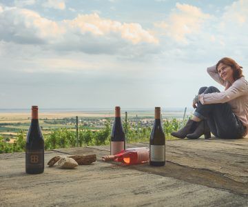 Woman seated outdoors, looking at bottles of wine on a stone surface overlooking Birgit Braunstein vineyard