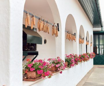 White arched veranda with pink flowers, hanging corn, and a black grill, at Birgit Braunstein