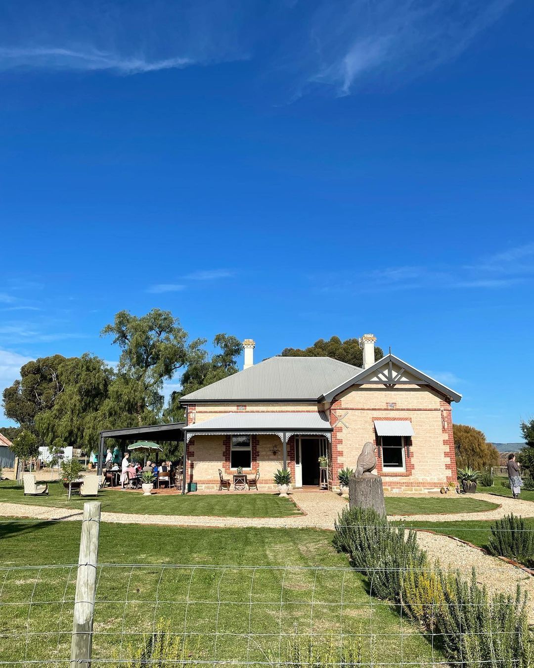 Stone house with veranda, green lawn, gravel path, and blue sky, at Bondar winery.