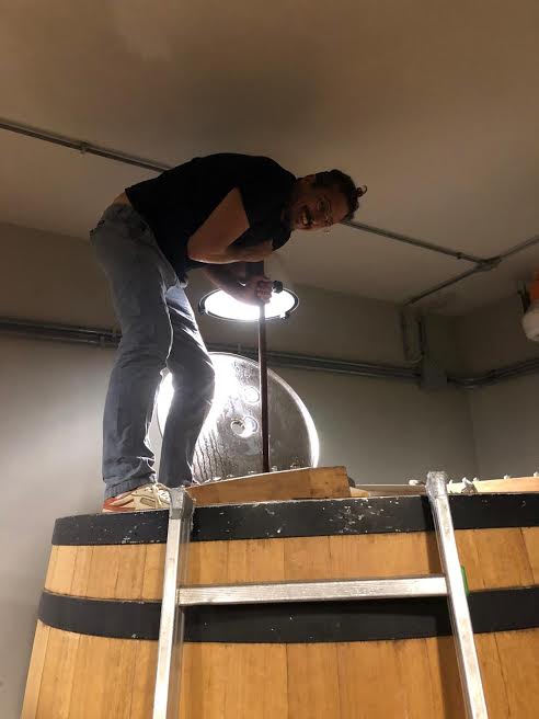 Winemaker of Casa Raia standing on a large wooden barrel, drilling.