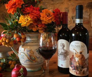 Casa Raia wine bottles and glass on a table with flowers and fruit