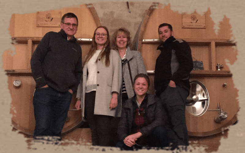 Team of Champagne Lelarge-Pugeot in front of large wooden wine vats, with one woman kneeling in the foreground.