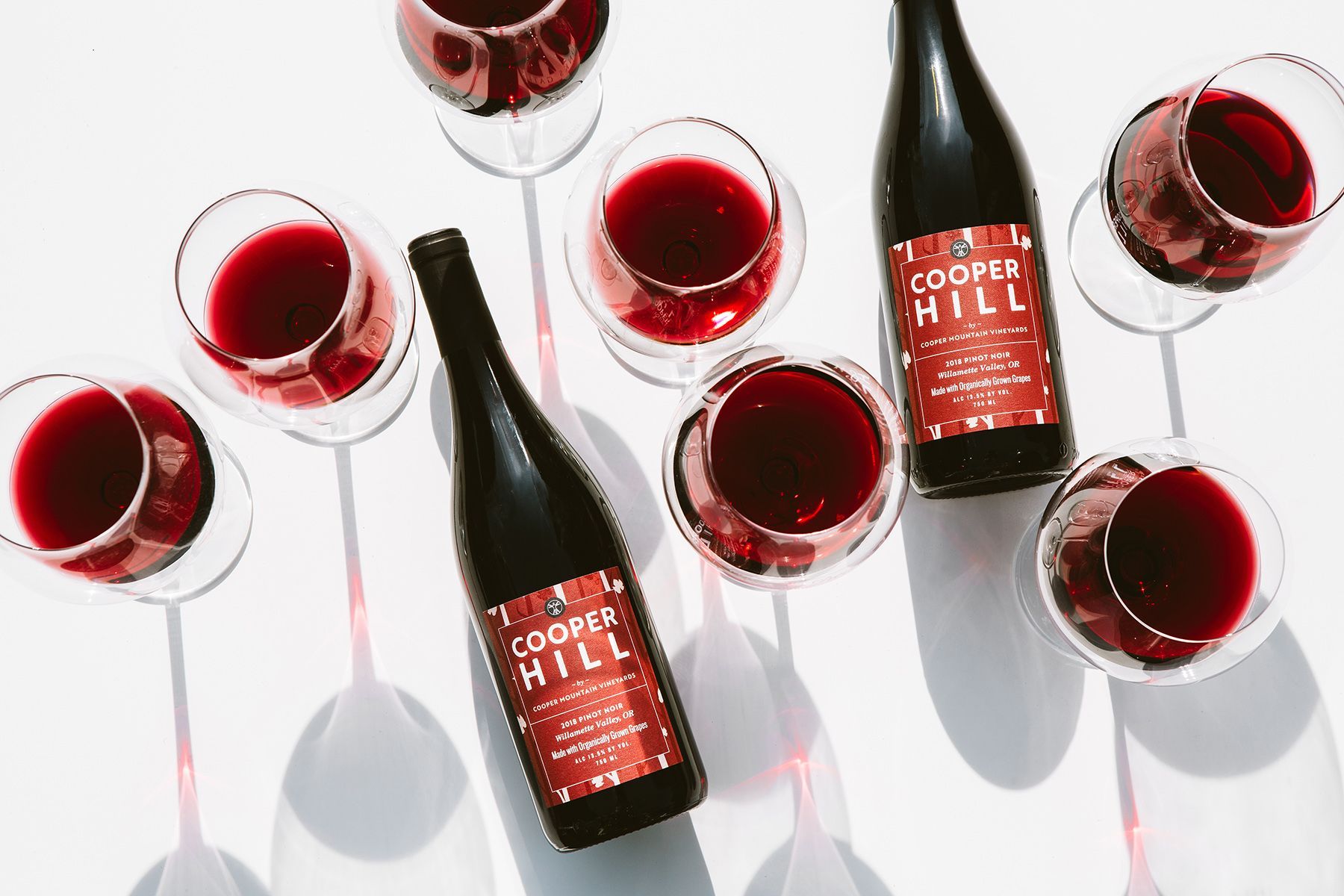 Bottles and glasses of red Cooper Mountain wine on a white surface.