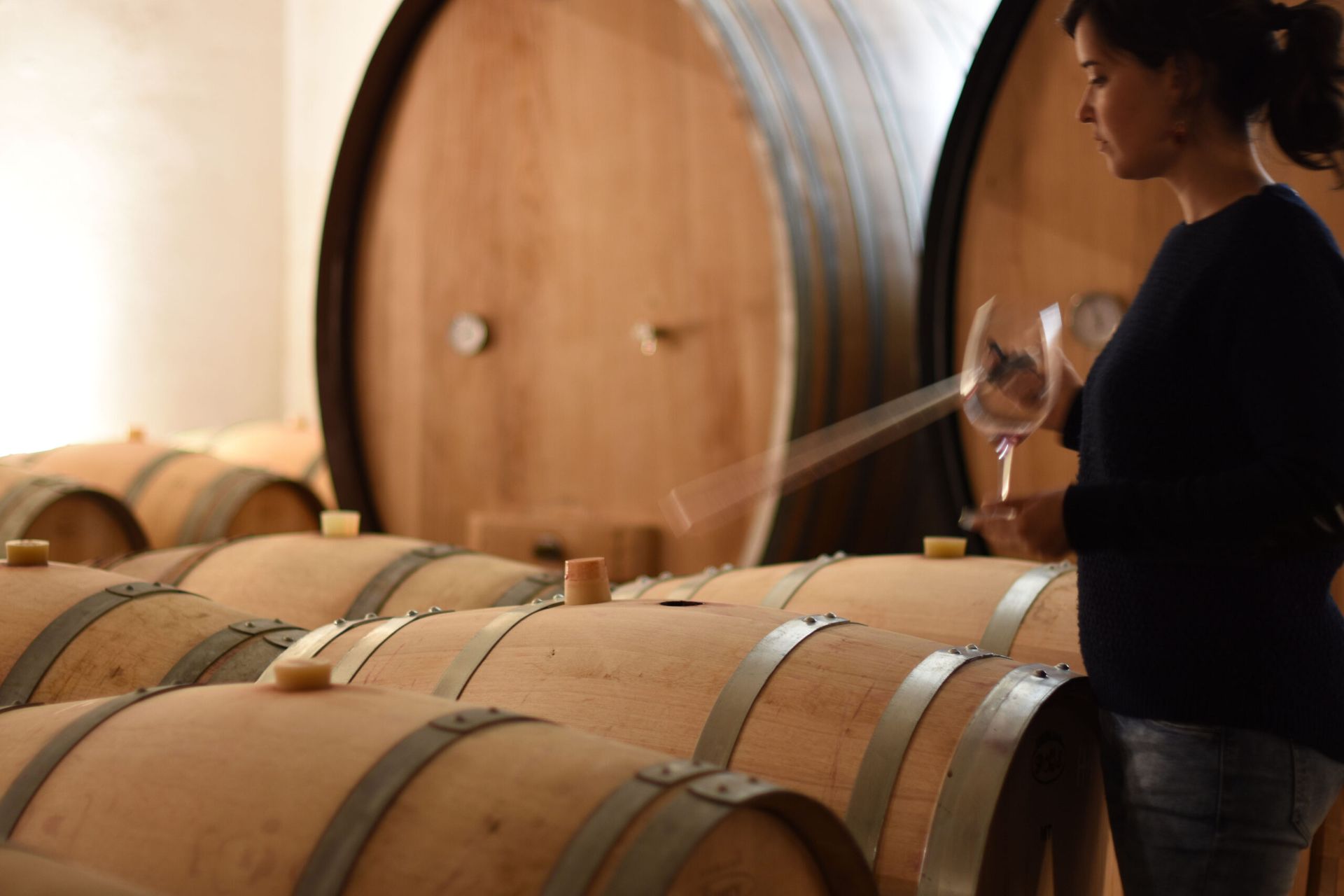 Woman in wine cellar holding a glass, inspecting barrels at Sierra de Toloño.
