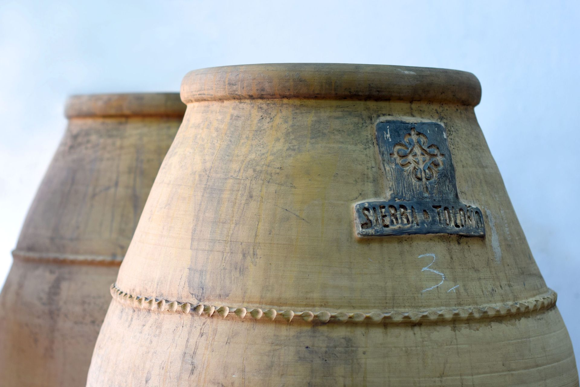 Two large, tan clay pots with the Sierra de Toloño logo.