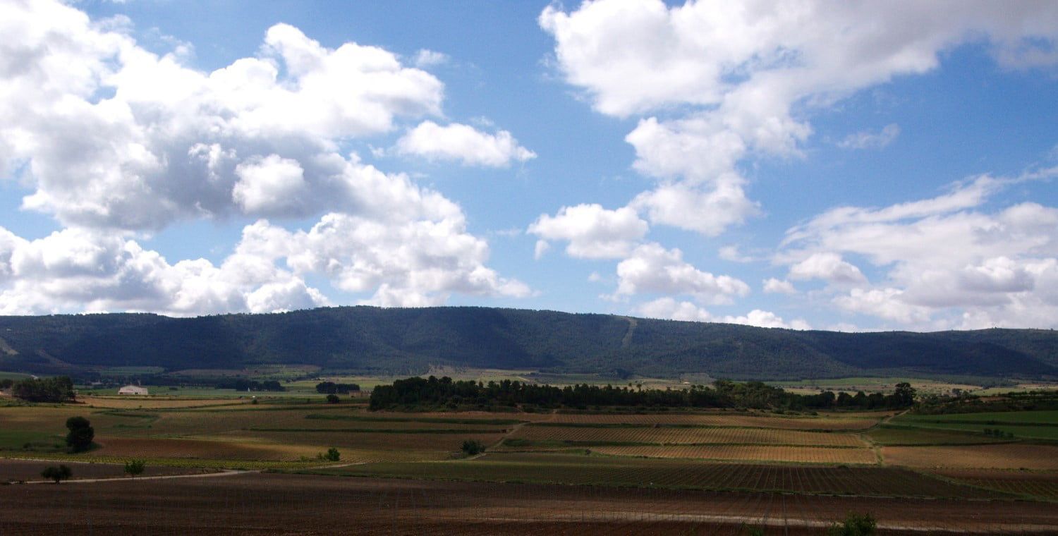 Blue sky with puffy clouds over a mountain range and fields, at Bodegas Enguera
