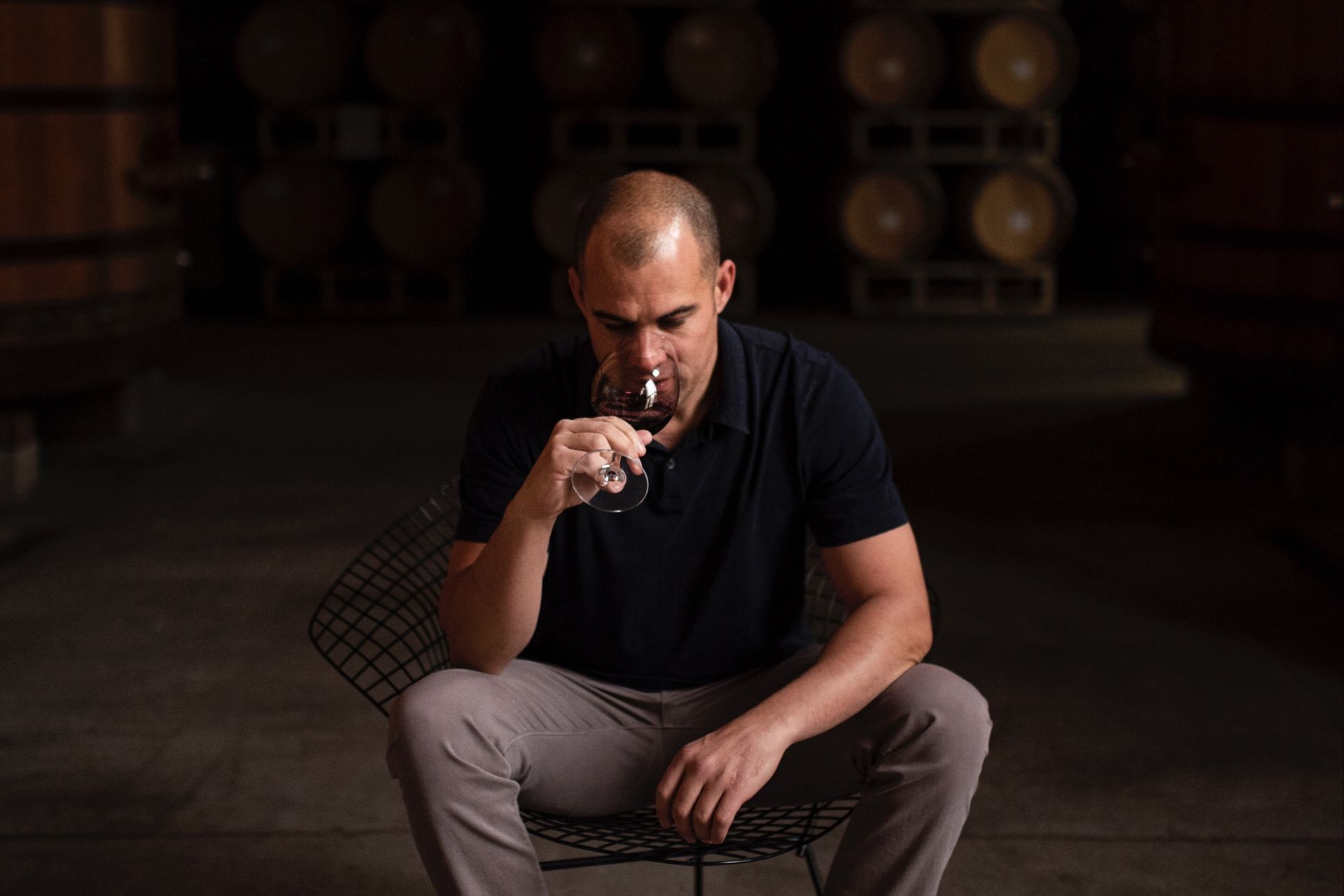 Winemaker of Grounded Wine Co sitting on a chair in the cellar, tasting a red wine.