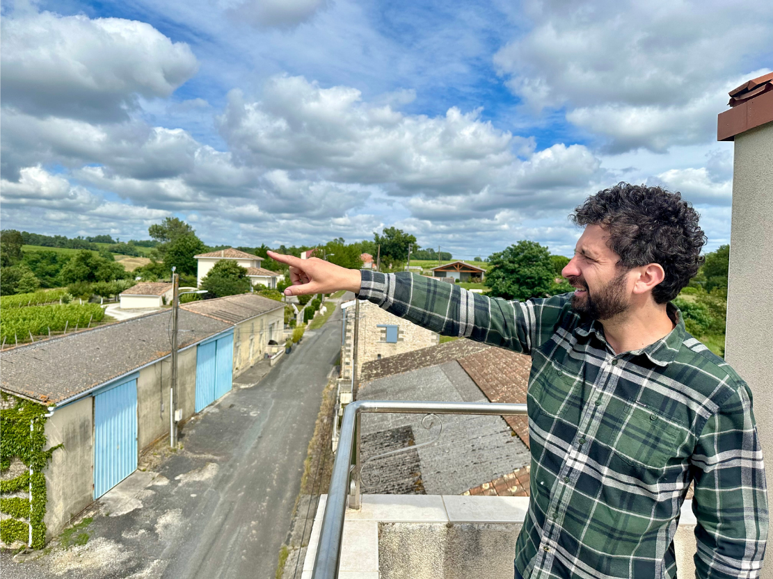 Château Haut Grelot winemaker pointing toward the vineyards from a rooftop.
