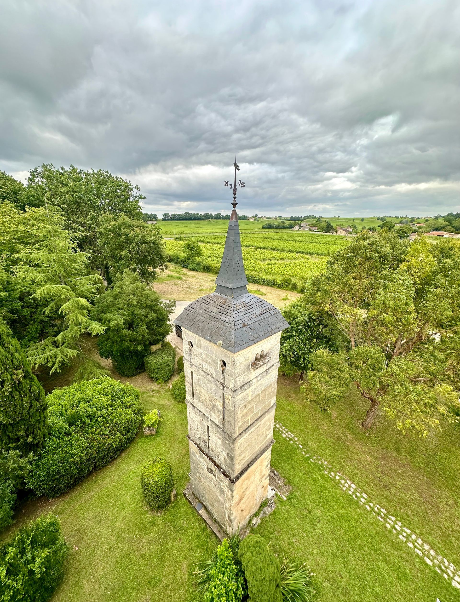 Peybonhomme-les-Tours - Stone tower with slate roof and weather vane, surrounded by green trees and fields.