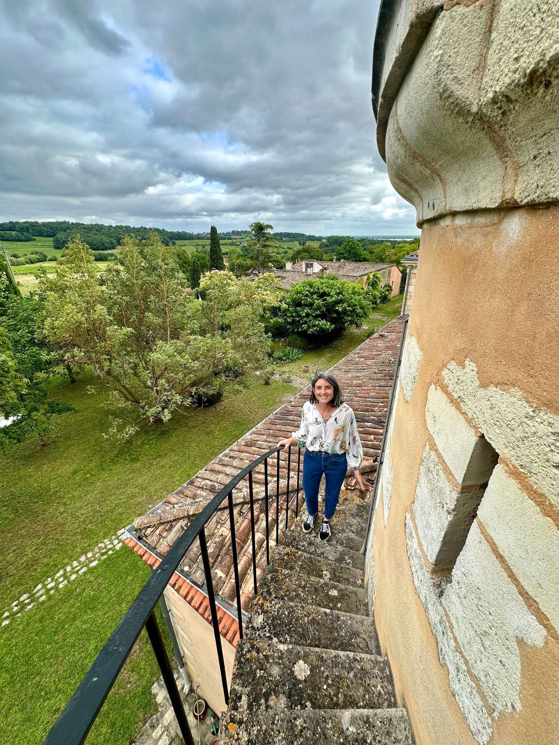 Peybonhomme-les-Tours - Woman on castle steps, smiling, overlooks green landscape under cloudy sky.