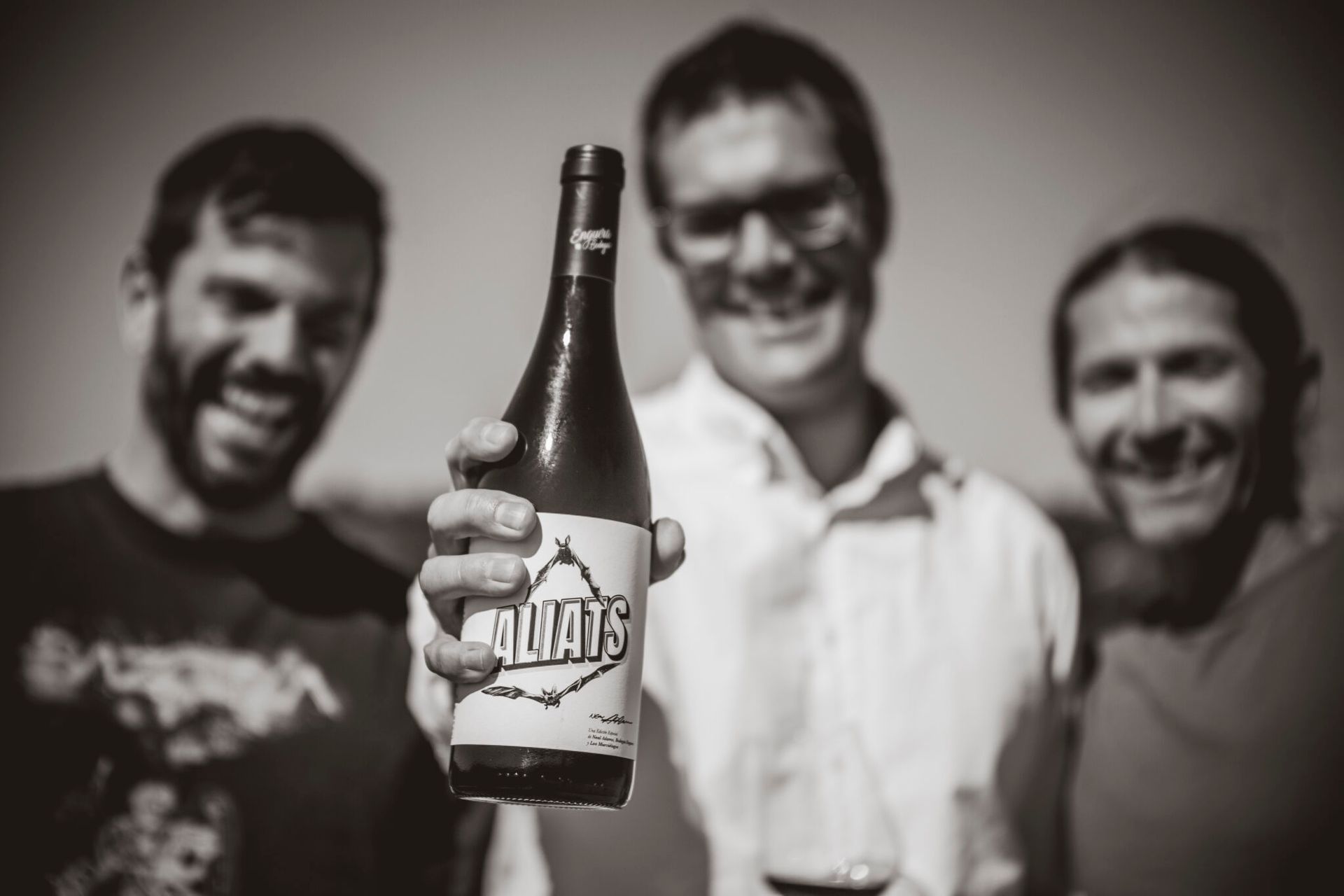 Three smiling men holding a wine bottle outdoors, at Bodegas Enguera