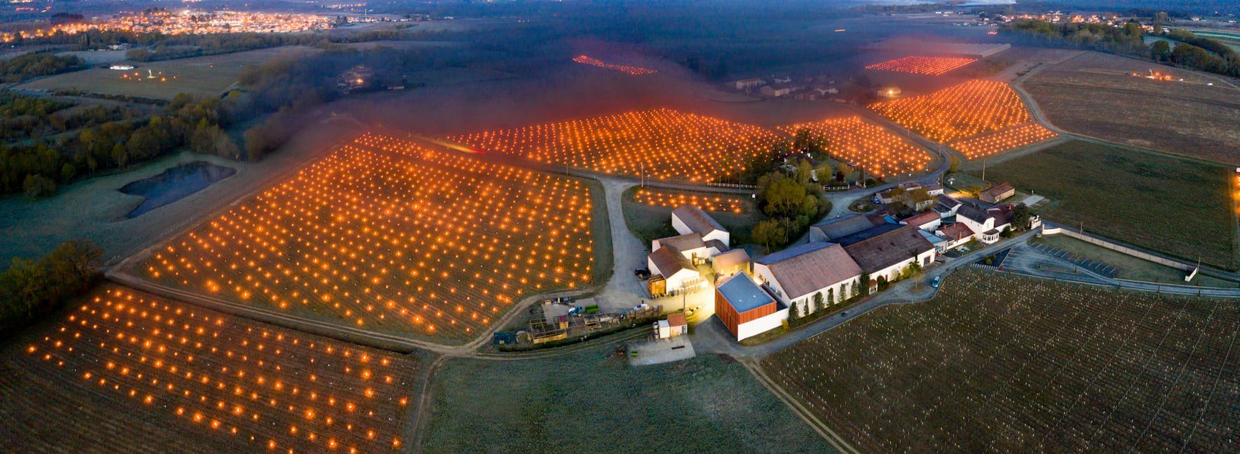 Aerial view of fields lit with small lights, near a building with brown roofs, at Luneau Papin