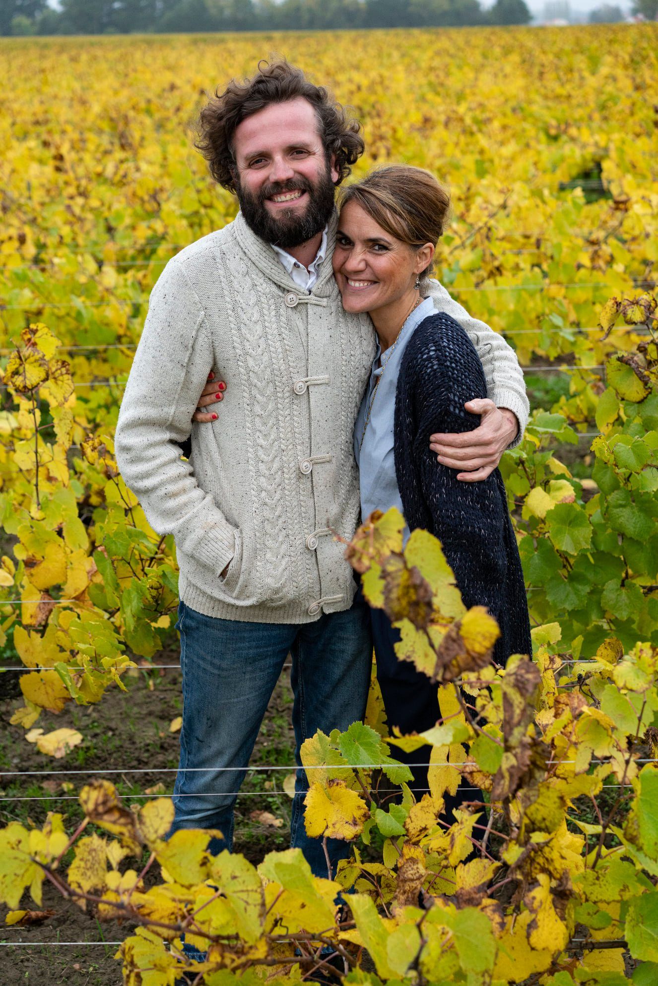 Couple embracing in a vineyard with yellow leaves, at Luneau Papin