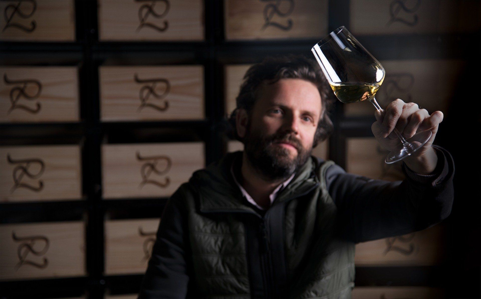 Winemaker of Luneau Papin examining wine in glass, holding it up, against backdrop of wine boxes.