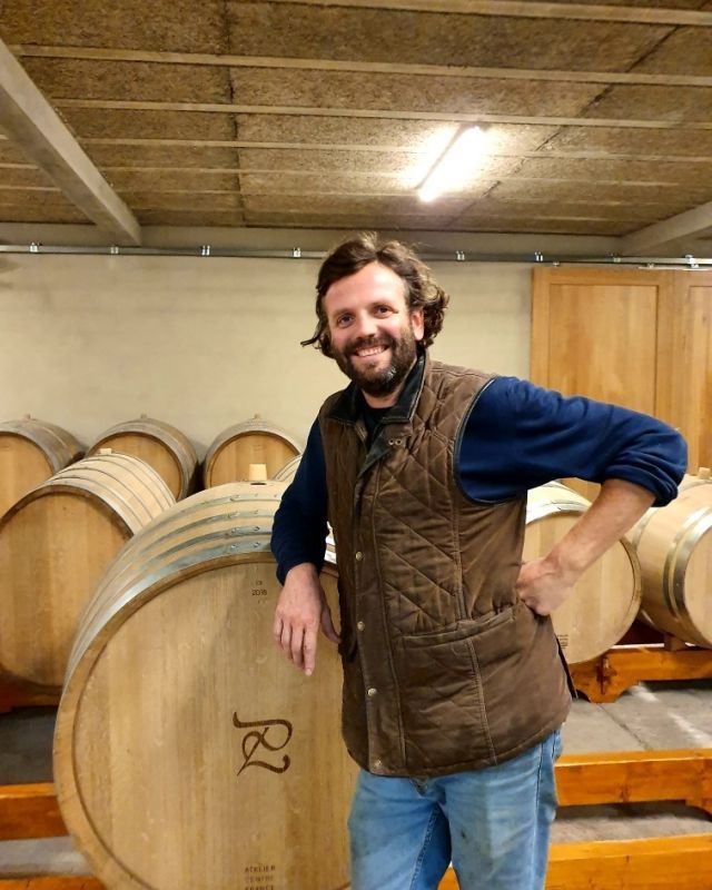 Winemaker of Luneau Papin leaning on a wine barrel in a cellar; smiling.
