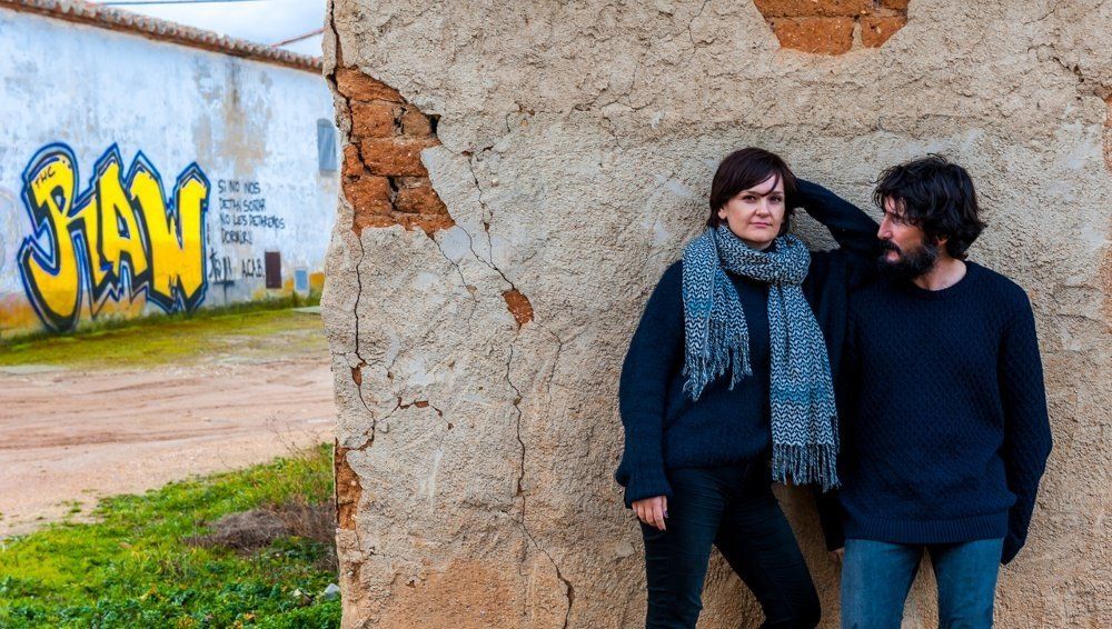 Couple leaning against a deteriorating wall at Máquina y Tabla with graffiti in the background.