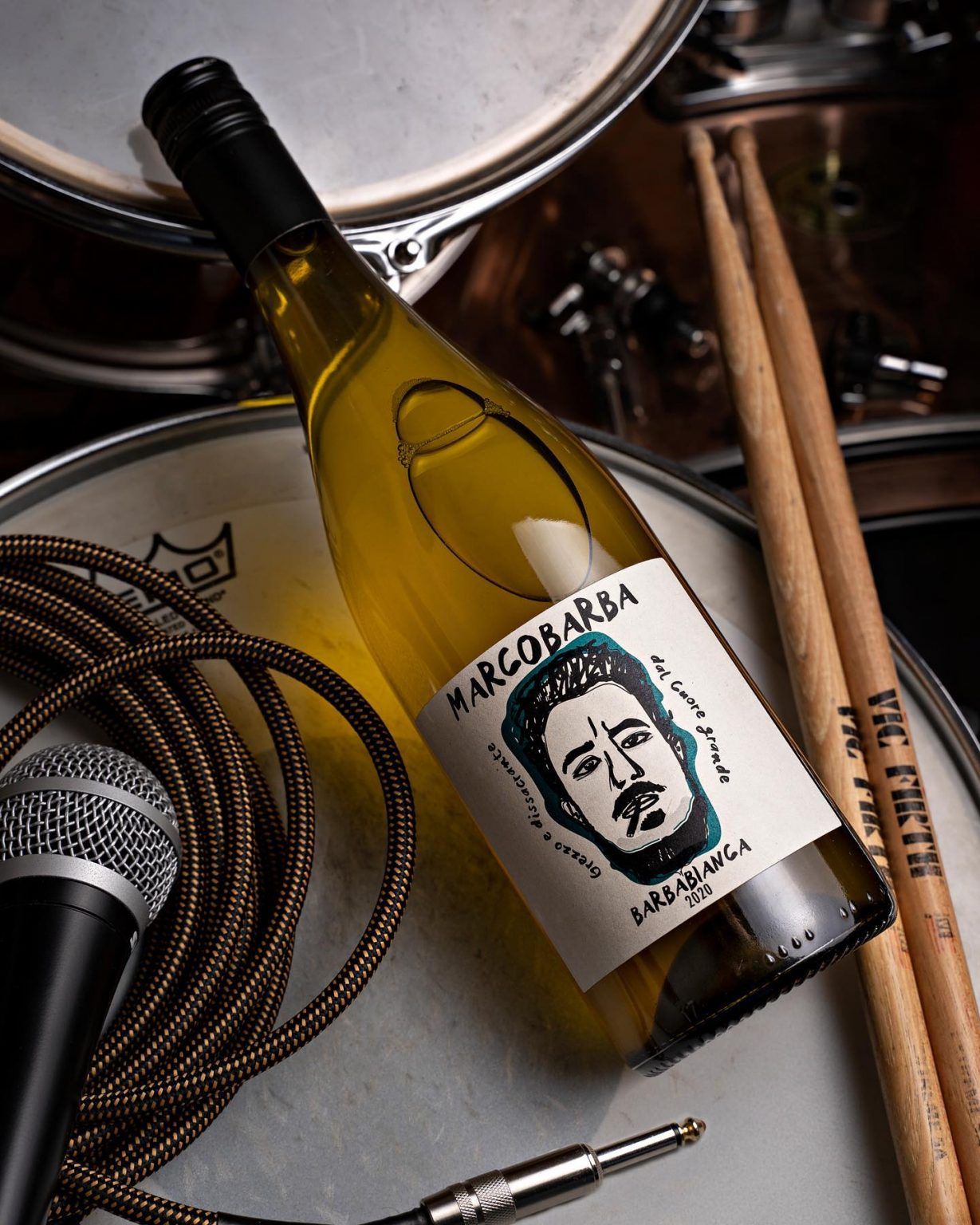 Marcobarba wine bottle on a drum set with drumsticks and a microphone.