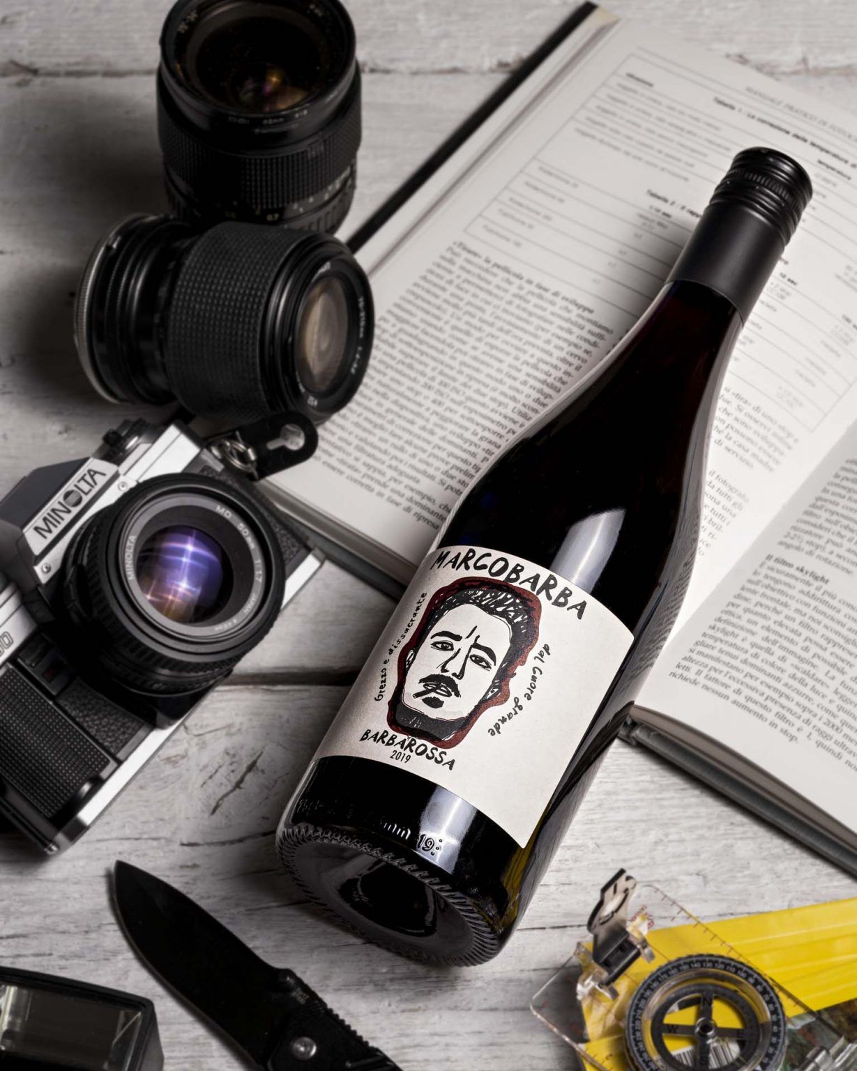 Bottle of Marcobarba Barbarossa red wine on a table with vintage cameras and open books.