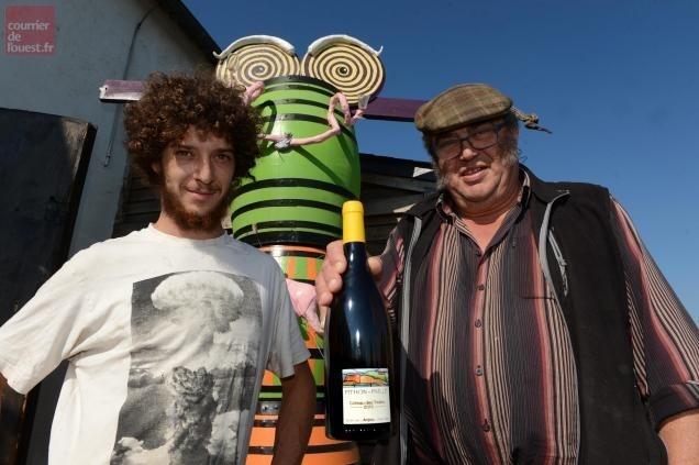 Two winemakers of Pithon-Paillé holding a wine bottle, standing by a colorful sculpture.