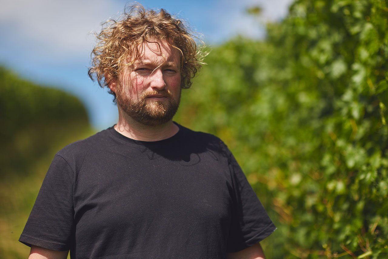 atrick Sullivan, wearing a black shirt, standing outside with green foliage in the background.