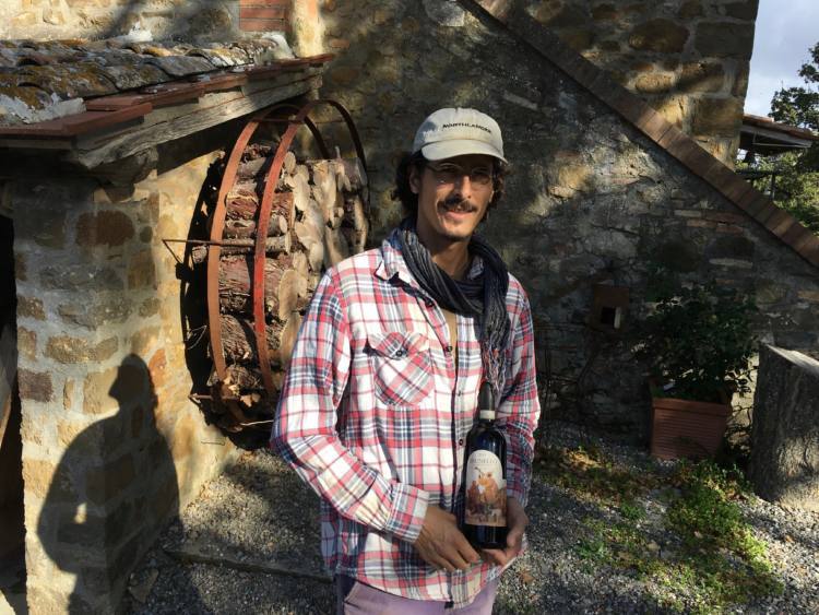 Winemaker of Casa Raia holding a wine bottle, standing near stone building