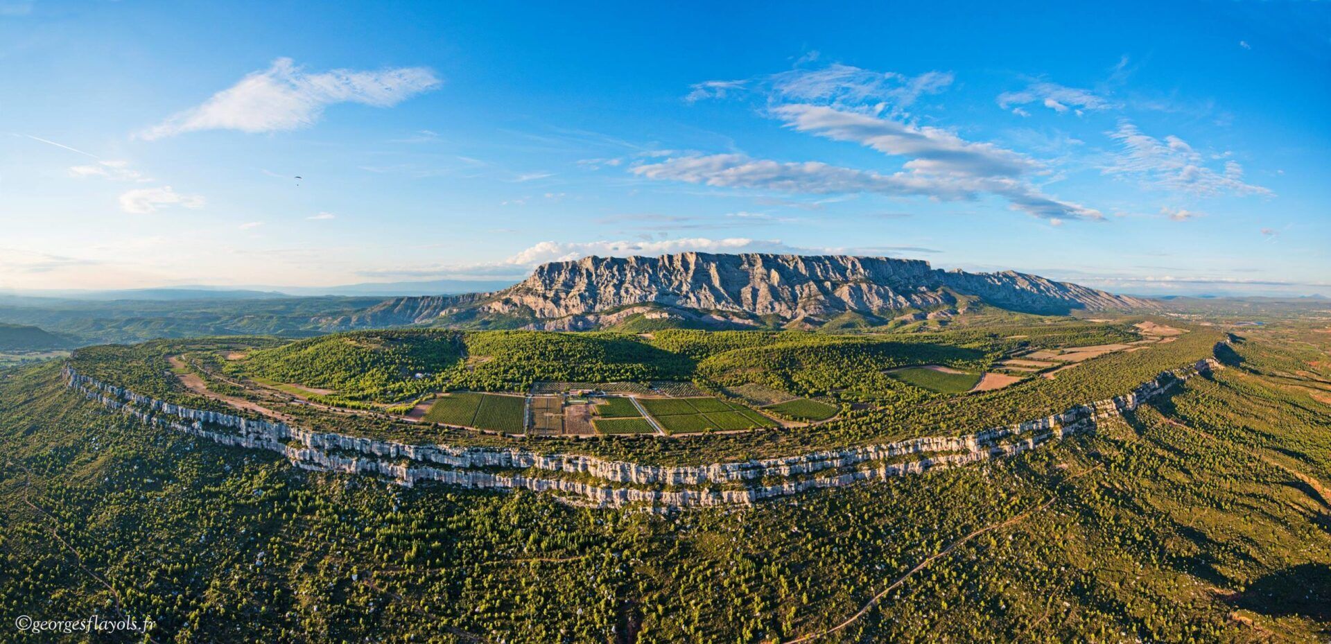 Panoramic view of a rocky mountain range and surrounding green landscape under a blue sky with clouds.