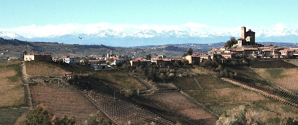 Panoramic view of a town on a hill with a castle and snow-capped mountains, at Rivetto