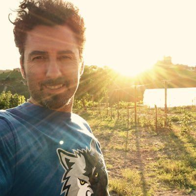 Man smiling in front of a sunny vineyard, at Rivetto