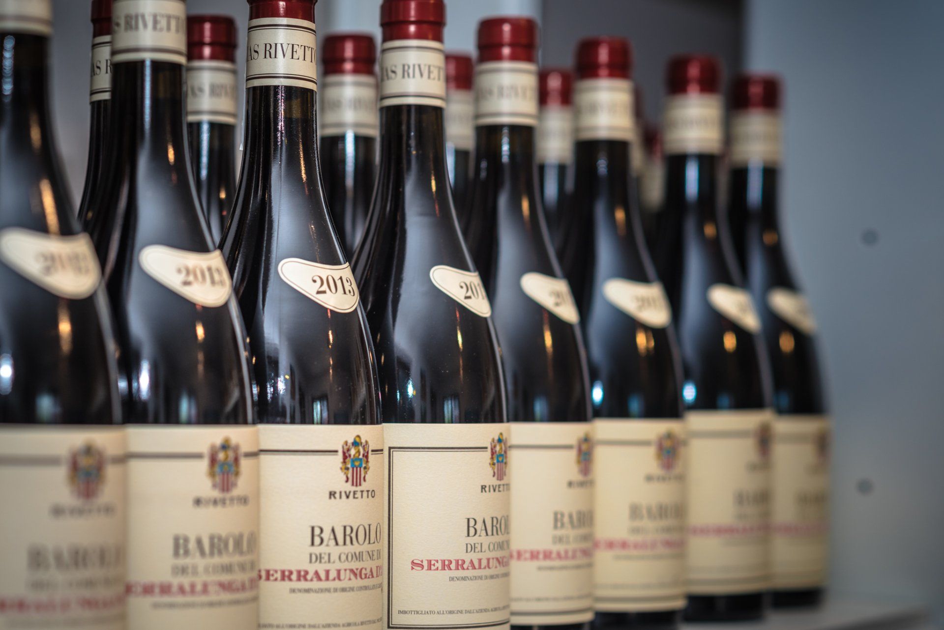 Row of wine bottles with white labels, red caps, and dark glass.