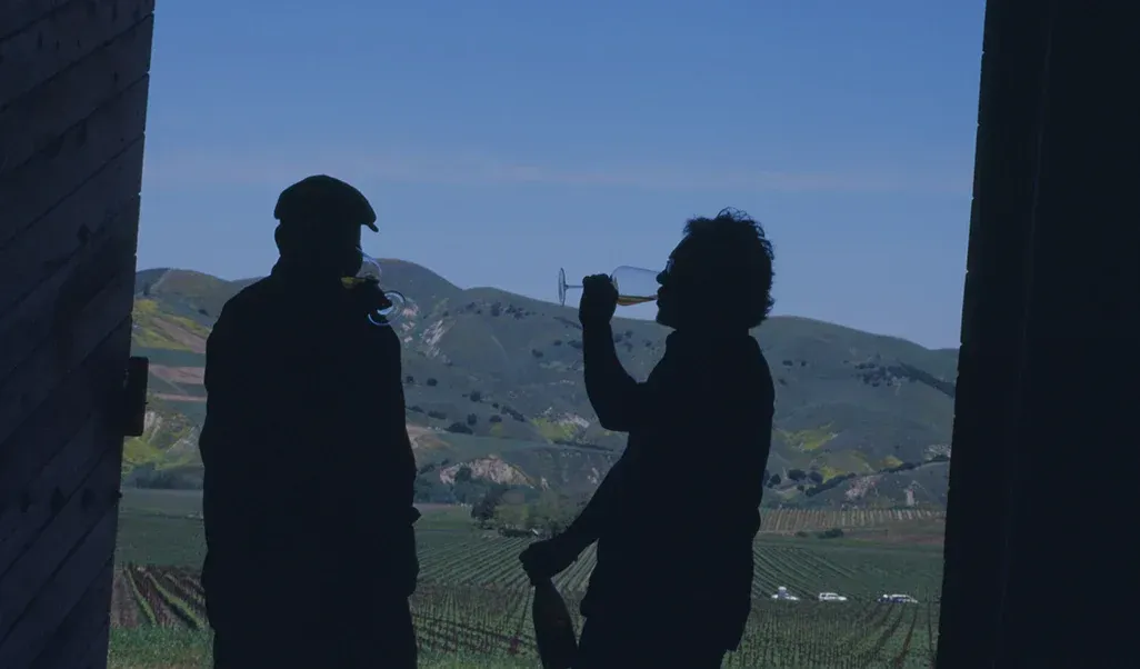 Silhouetted figures drinking wine in a doorway overlooking Sandhi vineyard