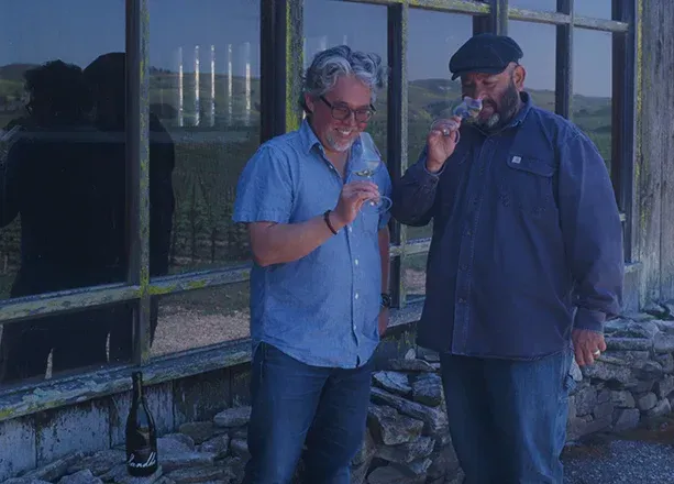 Two men examining wine in glasses outside Sandhi Winery