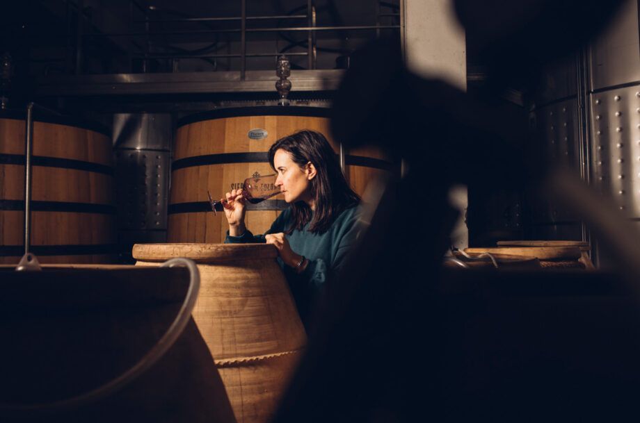 Woman tasting wine in a cellar, with wooden barrels on the background