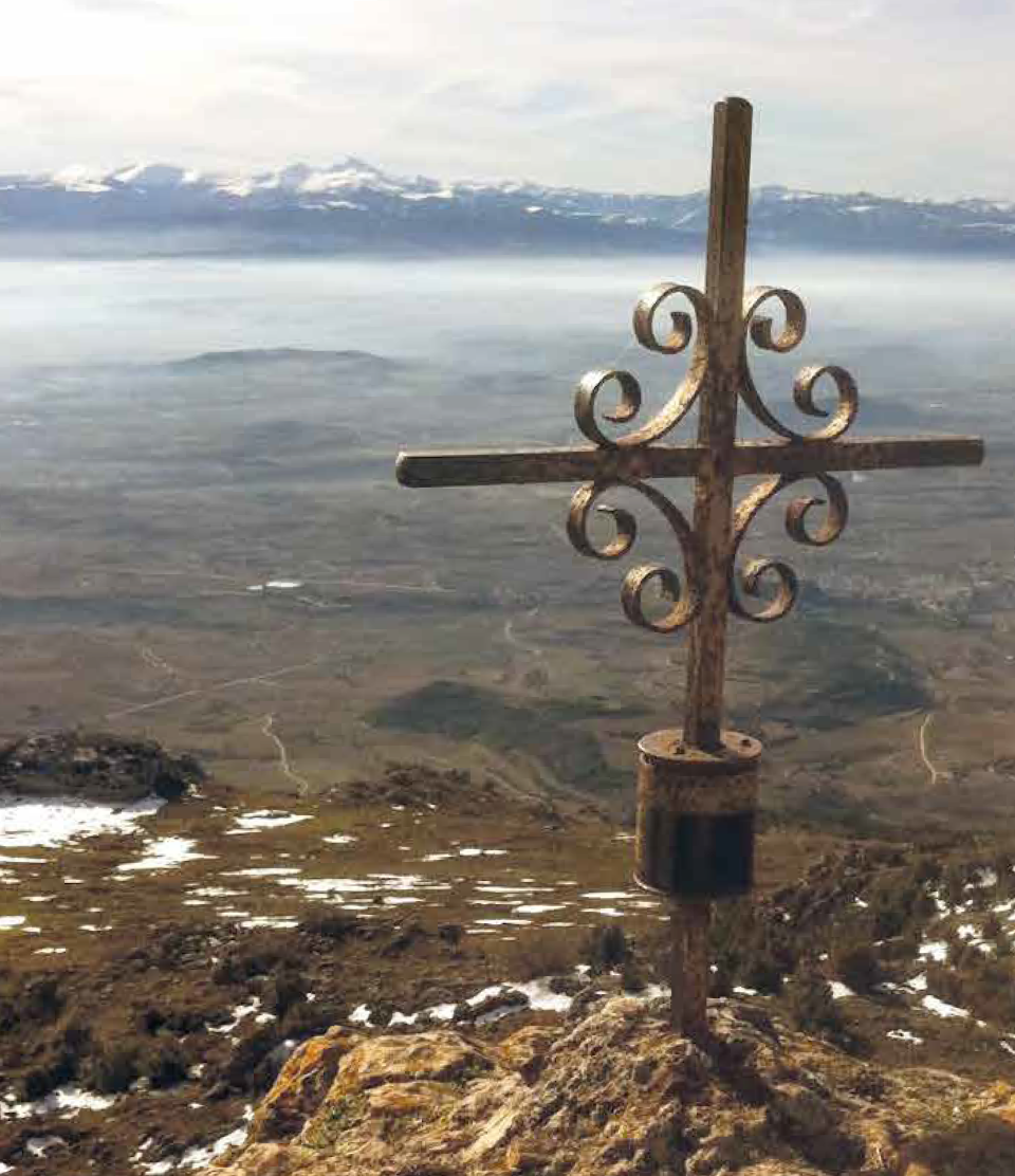 Metal cross on mountaintop, overlooking a hazy landscape, at Sierra de Toloño