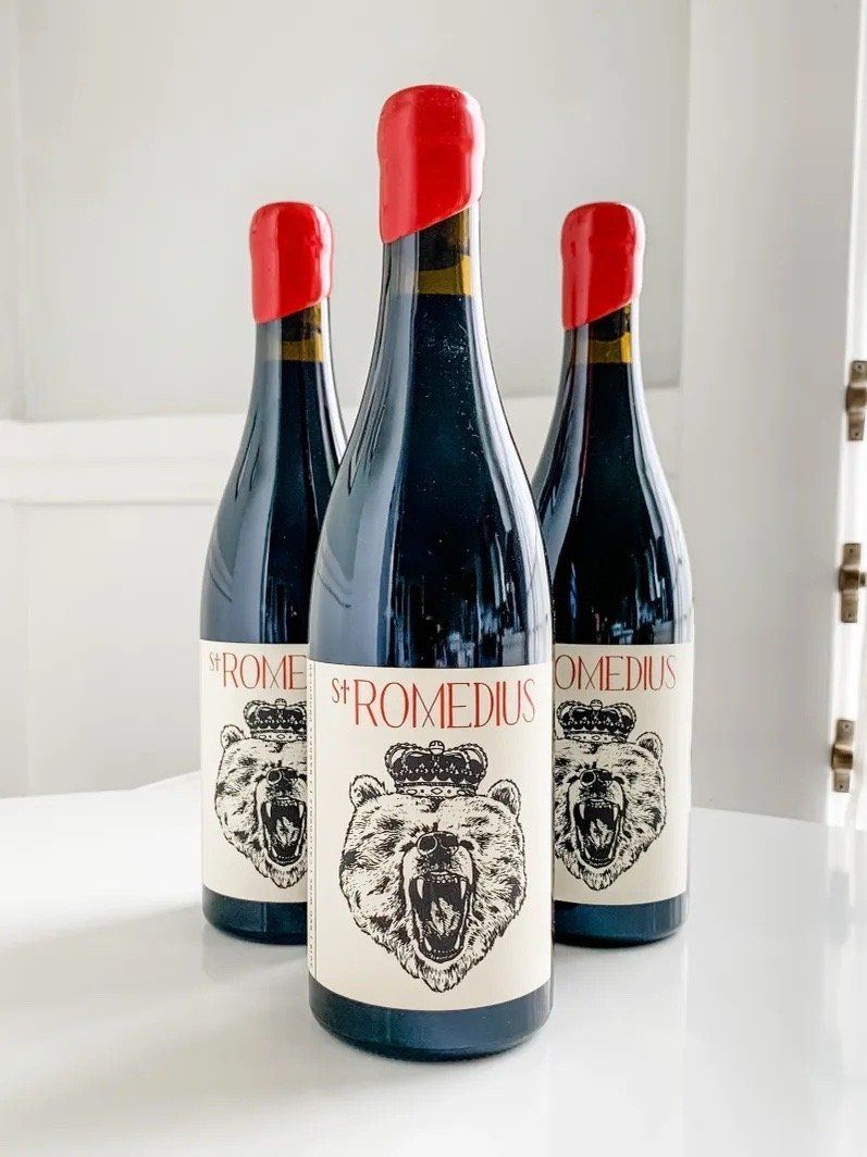 Three St. Romedius wine bottles with red wax seals and bear labels on a white surface.