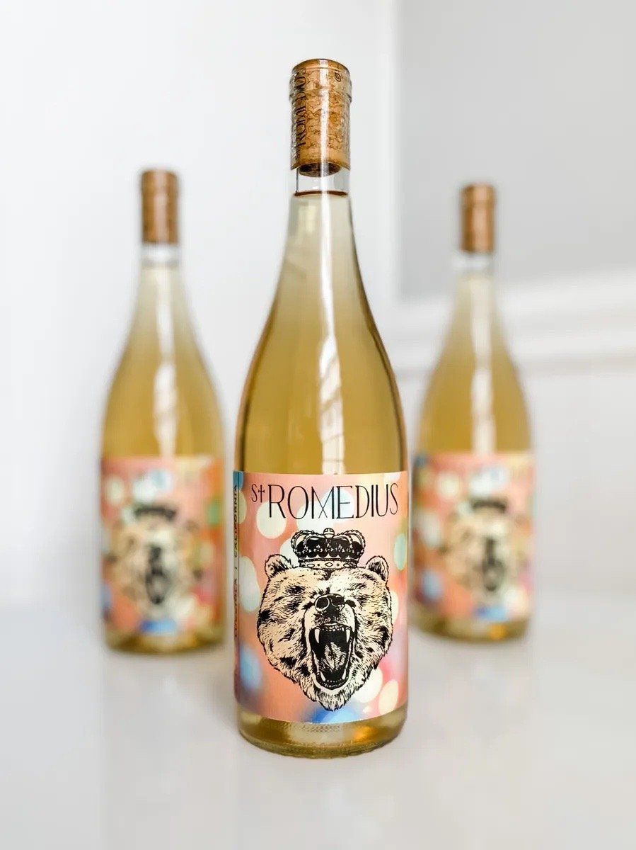 St. Romedius Lucciola white wine bottle with illustrated bear label, and two more bottles on the background.