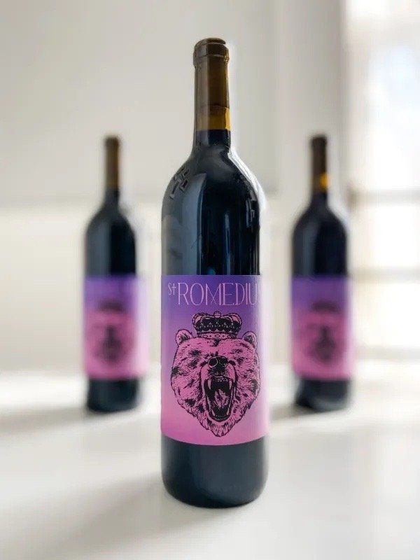 St. Romedius Teroldego bottle with illustrated bear label, two bottles softly blurred in the background.