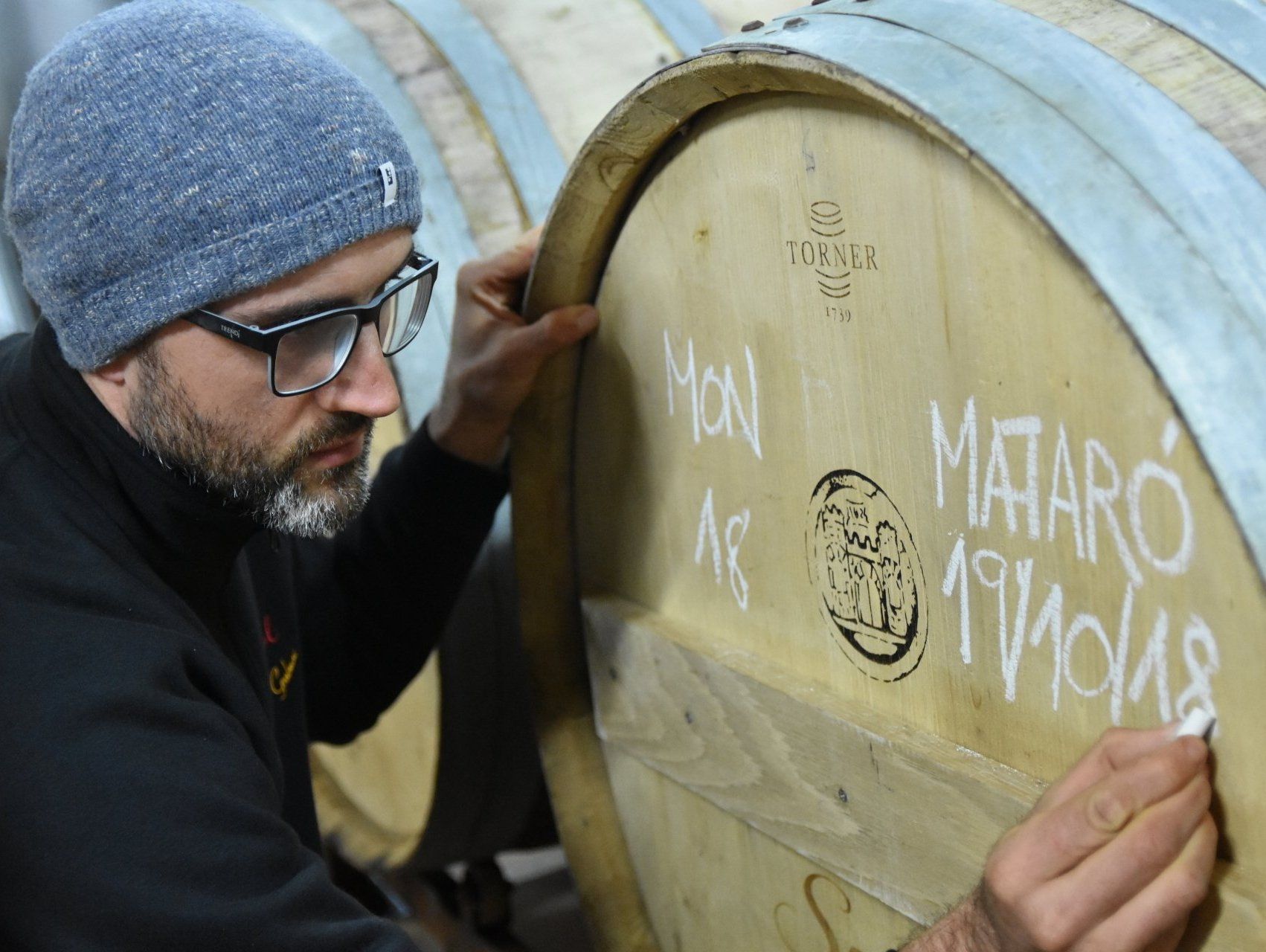 A Suriol winemaker marking a barrel labeled Mataró during cellar work.