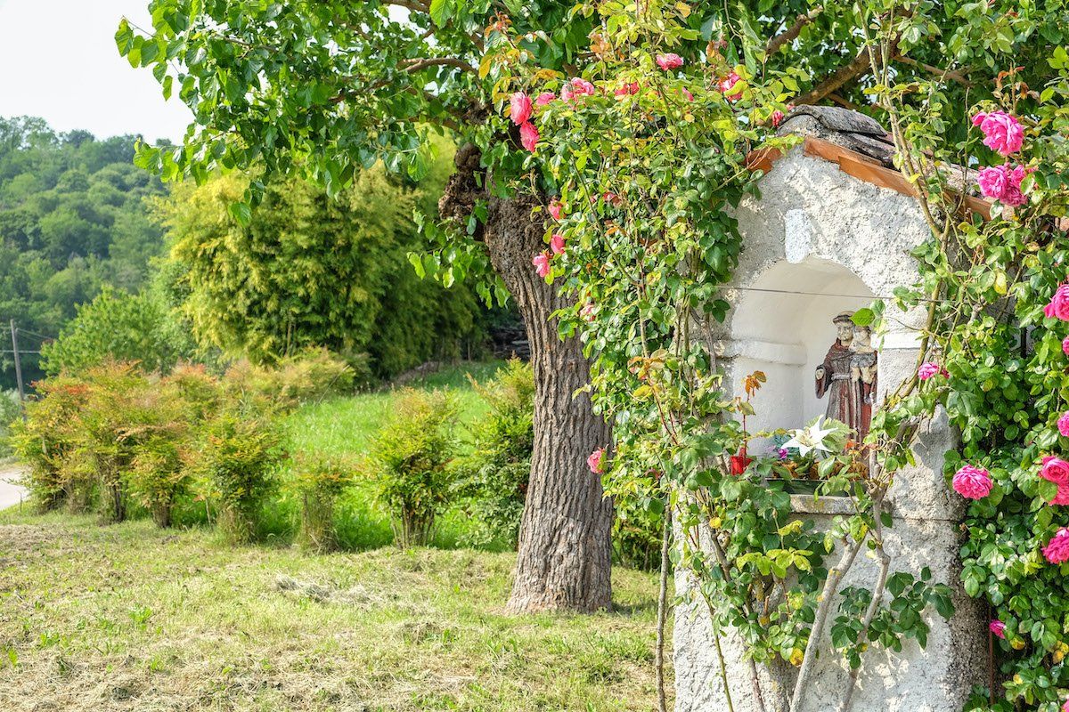 Stone shrine with statue and roses in grassy field at Tenuta Amadio vineyards
