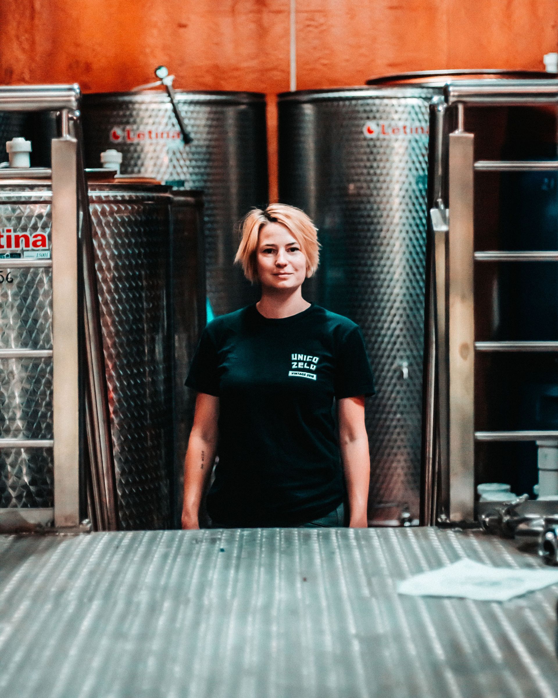 A Unico Zelo winemaker stands inside the winery, with stainless steel fermentation tanks in the background.