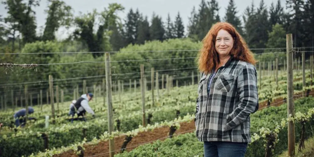 Winemaker standing in Evening Land vineyard with workers digging soil in the background