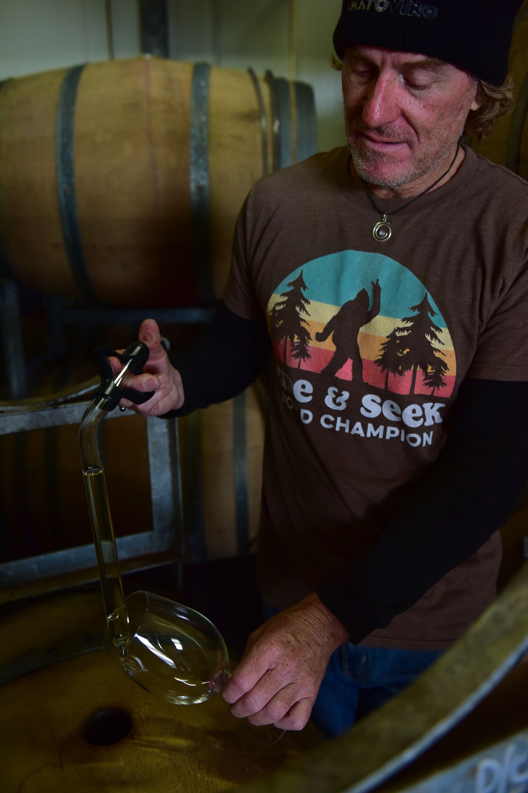 Winemaker drawing wine from a barrel using a wine thief in the cellar.
