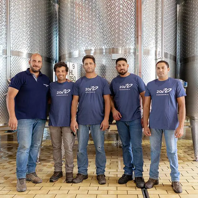 Di Giovanna team stand in the winery, posing in front of large metal tanks.