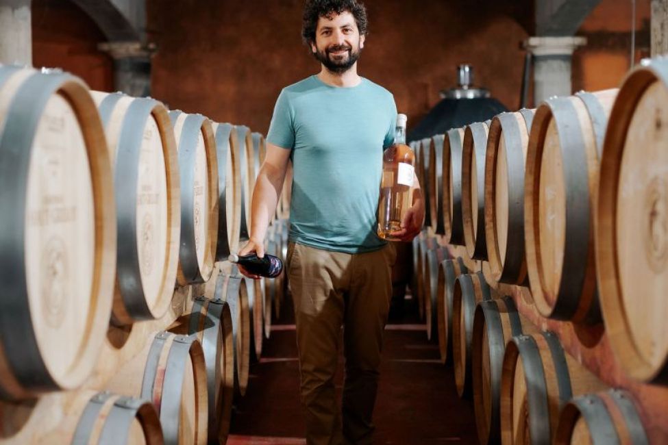Château Haut Grelot winemaker in the cellar holding wine bottles among oak barrels.